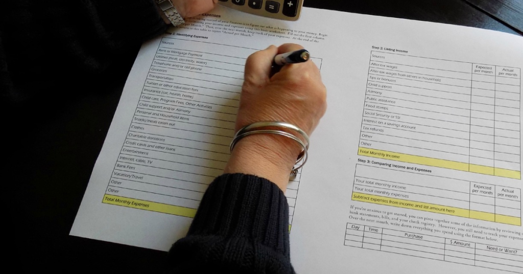 Woman with a silver bracelet writing on a budget worksheet.