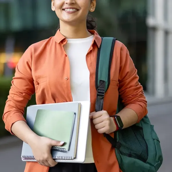 Female college student carrying a stack of notebooks with a backpack over one shoulder.