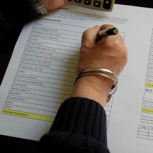 Woman with a silver bracelet writing on a budget worksheet.