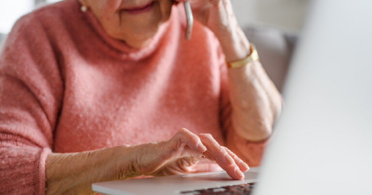Elderly woman on the phone while looking at her laptop