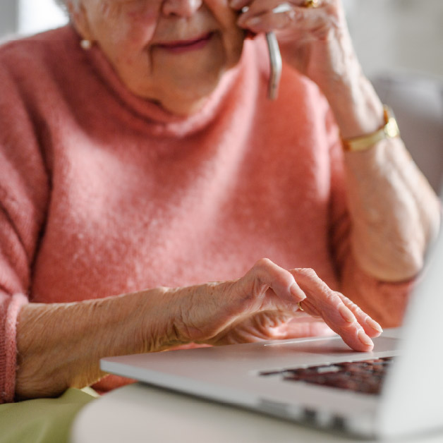 Elderly woman on the phone while looking at her laptop