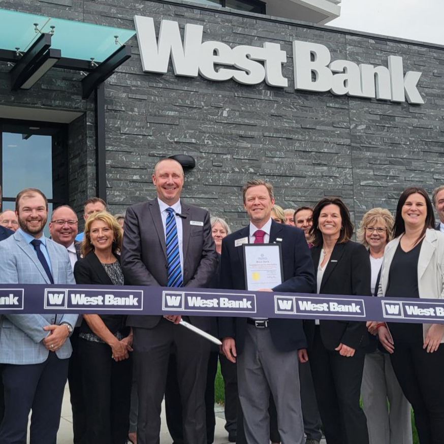 West Bank's Owatonna team, construction groups, and Owatonna Chamber team and ambassadors stand in front of the new West Bank building for a ribbon cutting.