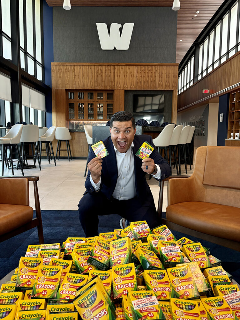 Gabe Olson posing in West Bank Headquarters with hundreds of boxes of crayons.
