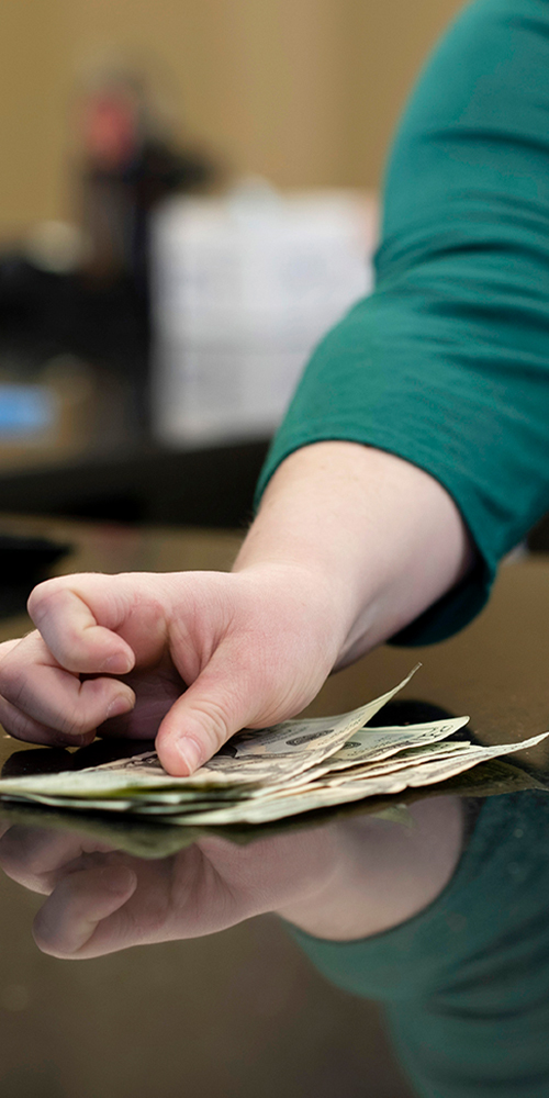 Woman in green shirt counting out cash on a counter.