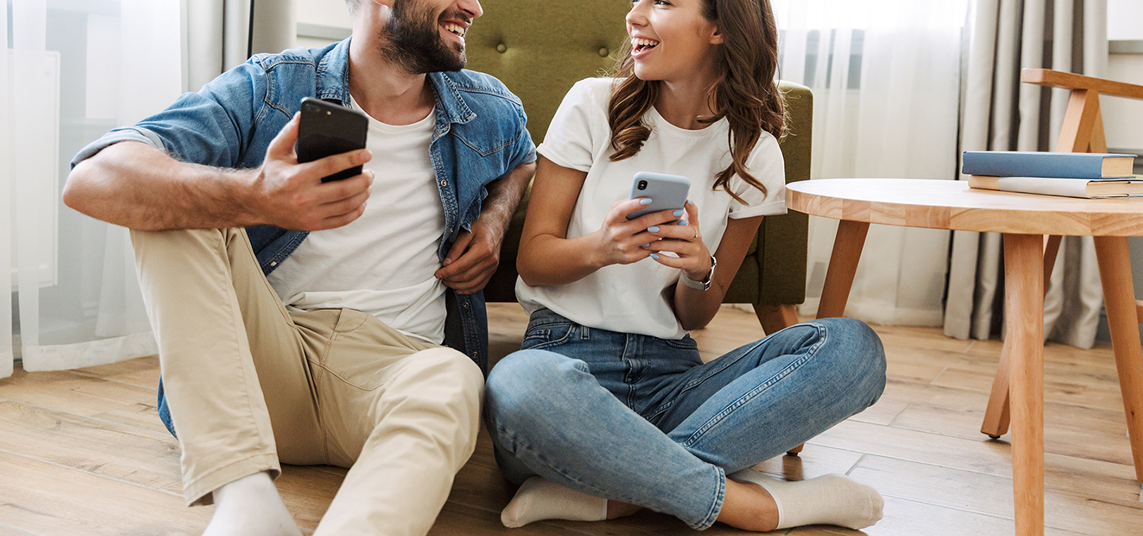 Beautiful young couple in love at home, sitting at the living room, using mobile phones