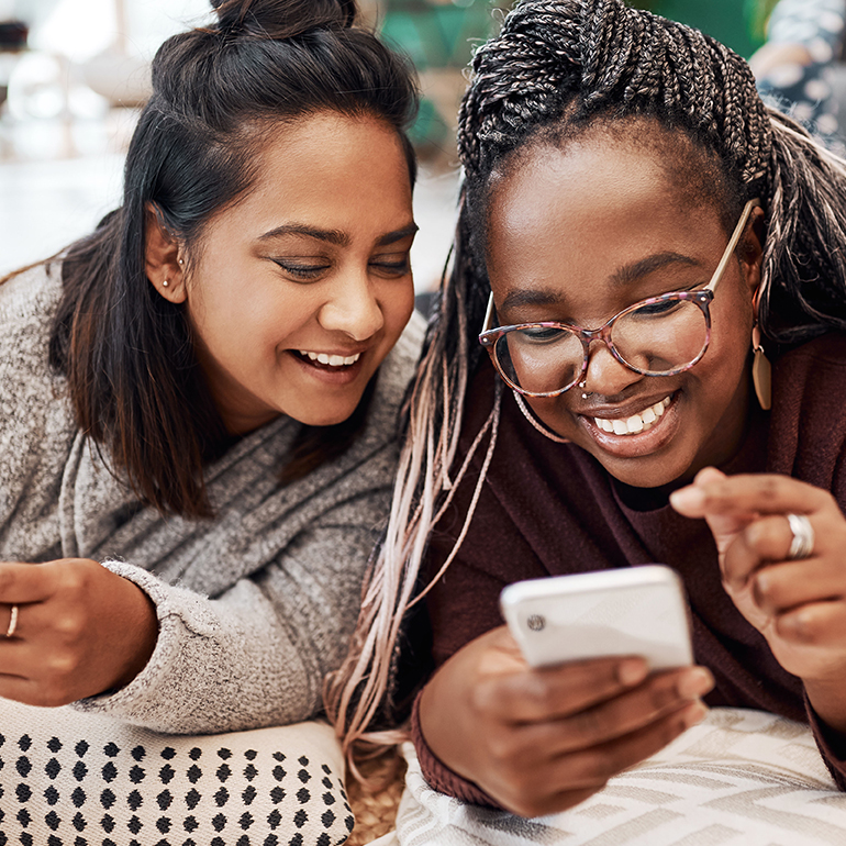 Shot of two young women using their smartphones on the floor at home.