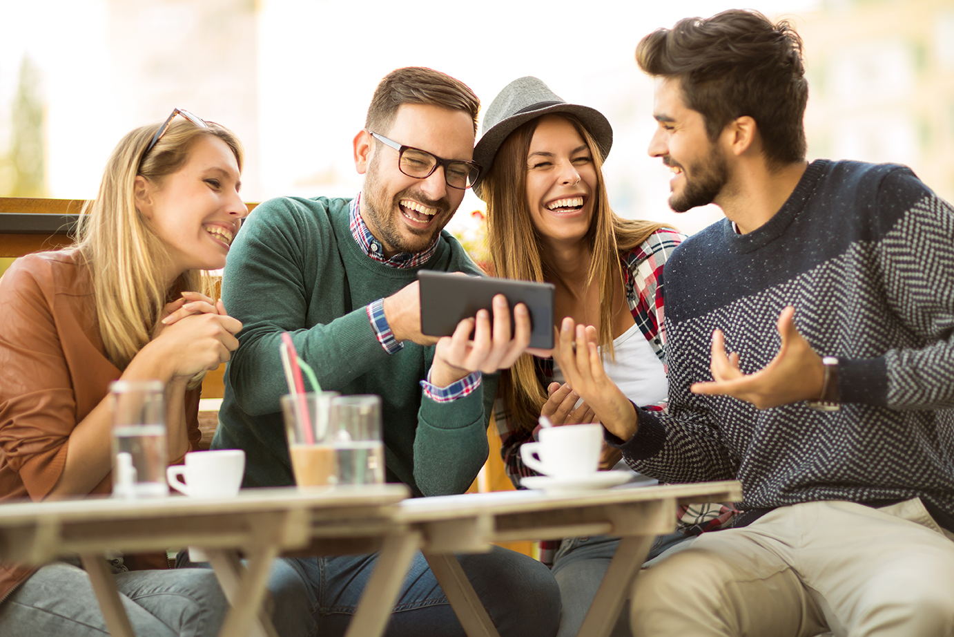 Two women and two men at cafe talking laughing and enjoying their time looking at a mobile phone.