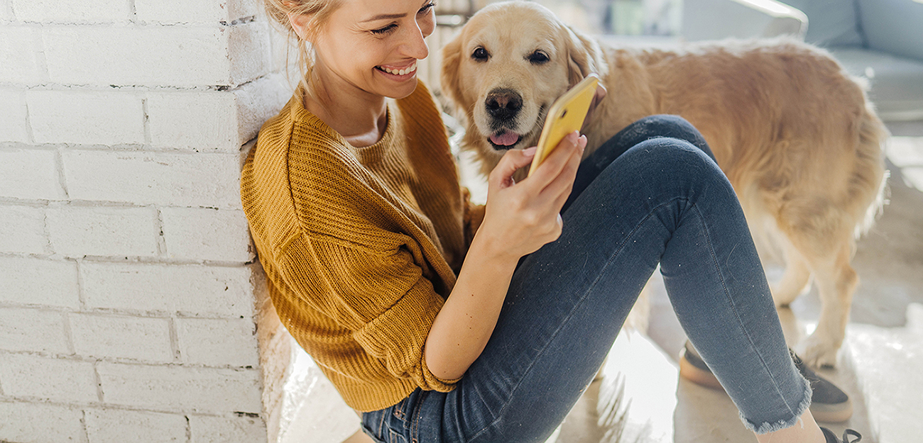 Photo of a young woman looking at her mobile phone while her dog standing next to her
