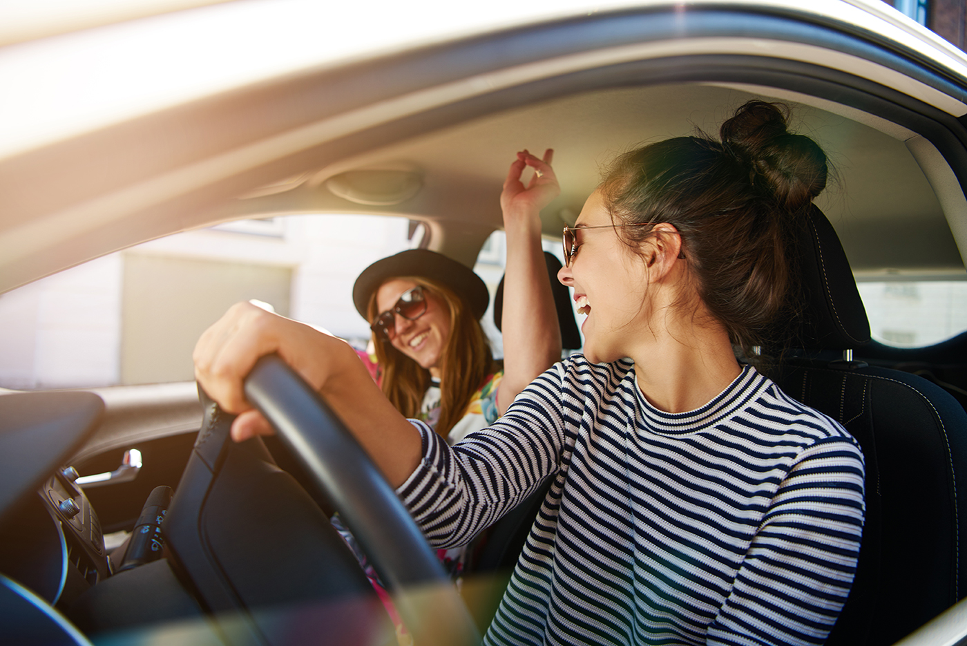 Two young women having fun driving along the street laughing.