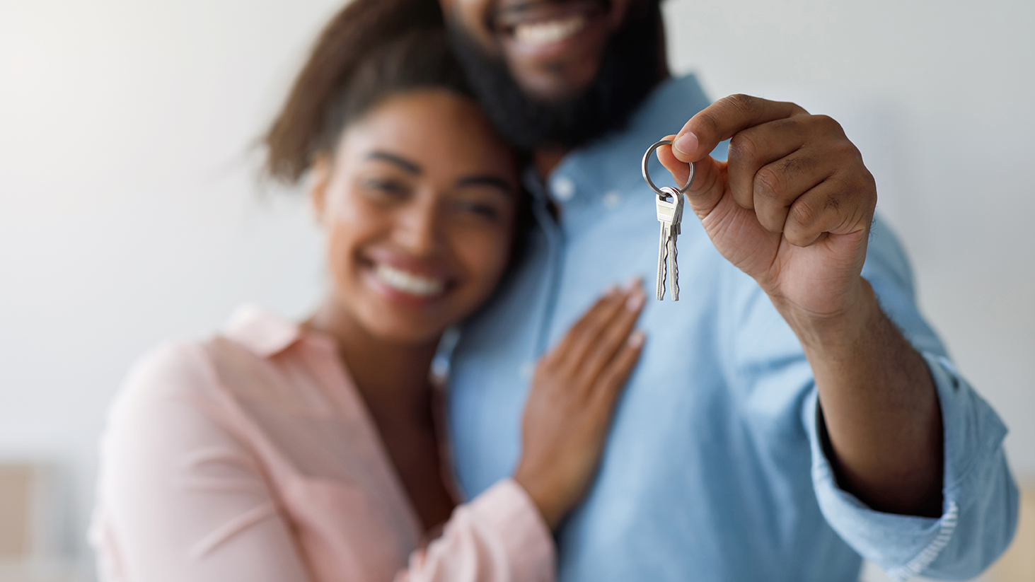 Millennial black couple hugging, showing keys to new house.