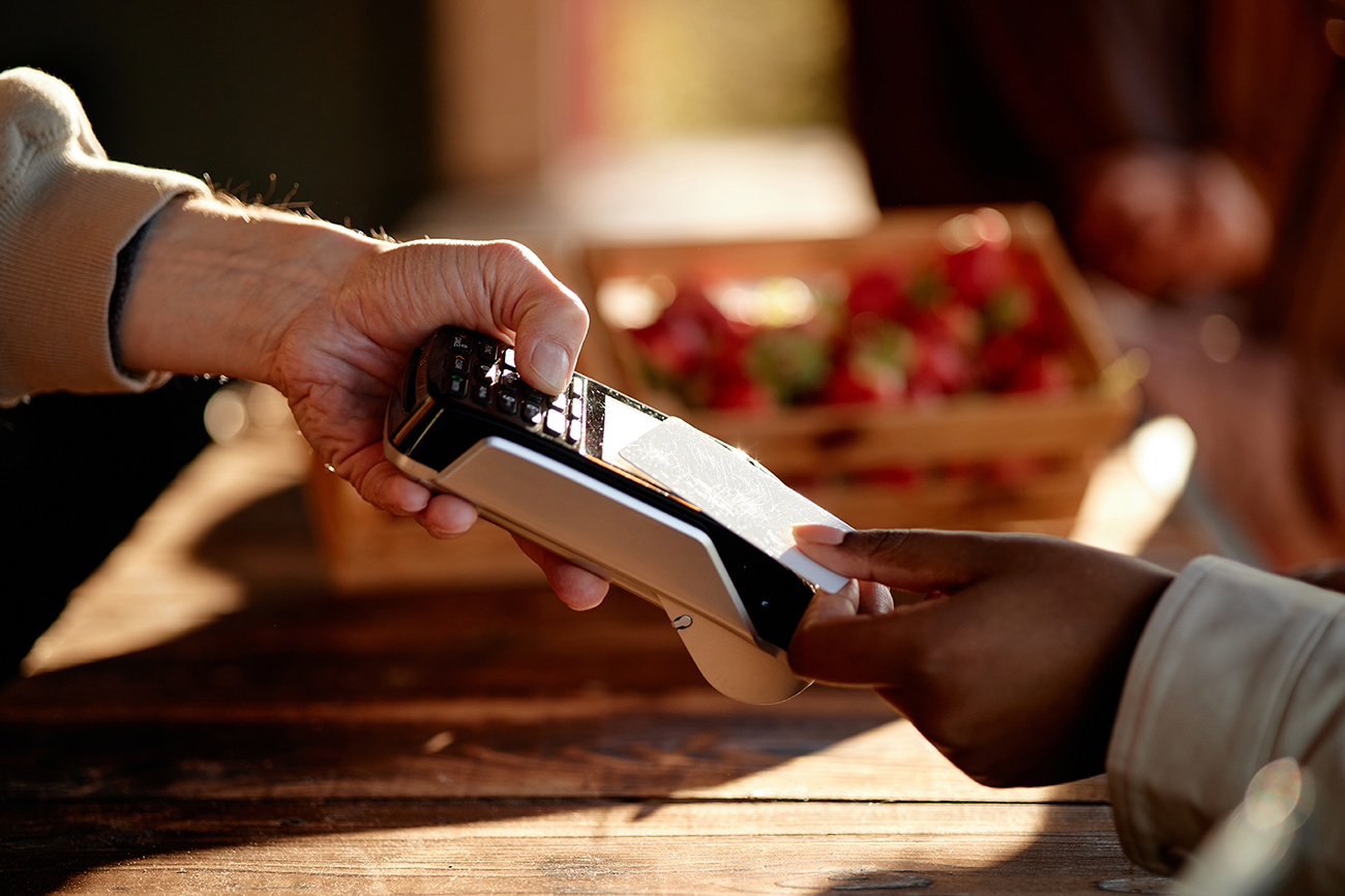 Caucasian man holding payment terminal while Black young adult woman making contactless payment.