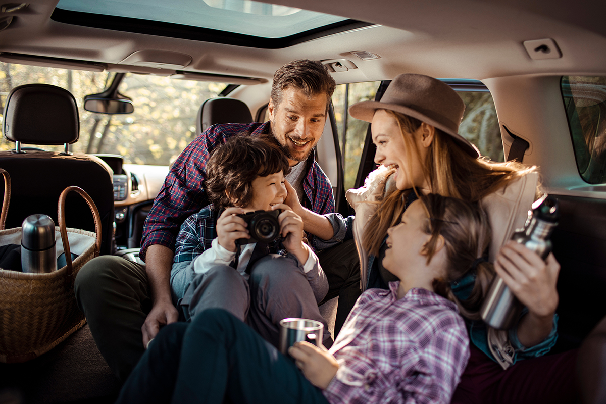 Family enjoying a road trip inside their car with kids taking photos and drinking from thermos