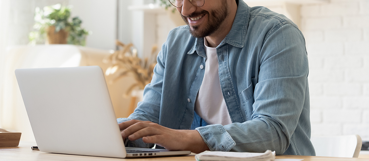 Male typing on laptop keyboard and smiling.