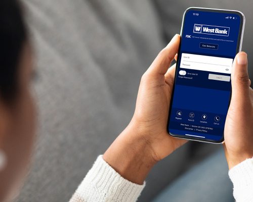 Woman Holding Smartphone with West Bank Mobile Banking login screen open.