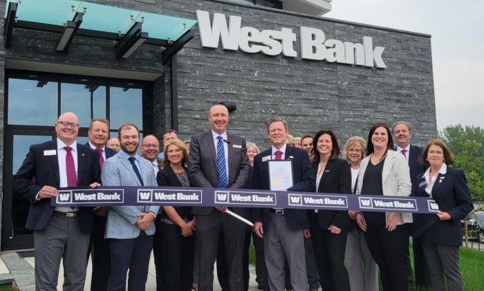 West Bank's Owatonna team, construction groups, and Owatonna Chamber team and ambassadors stand in front of the new West Bank building for a ribbon cutting.