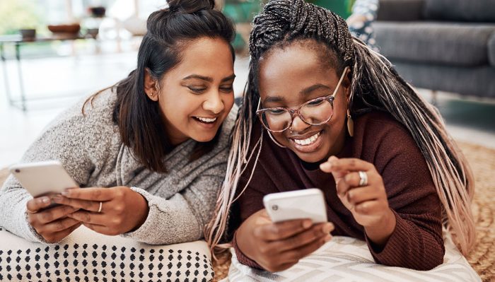 Shot of two young women using their smartphones on the floor at home